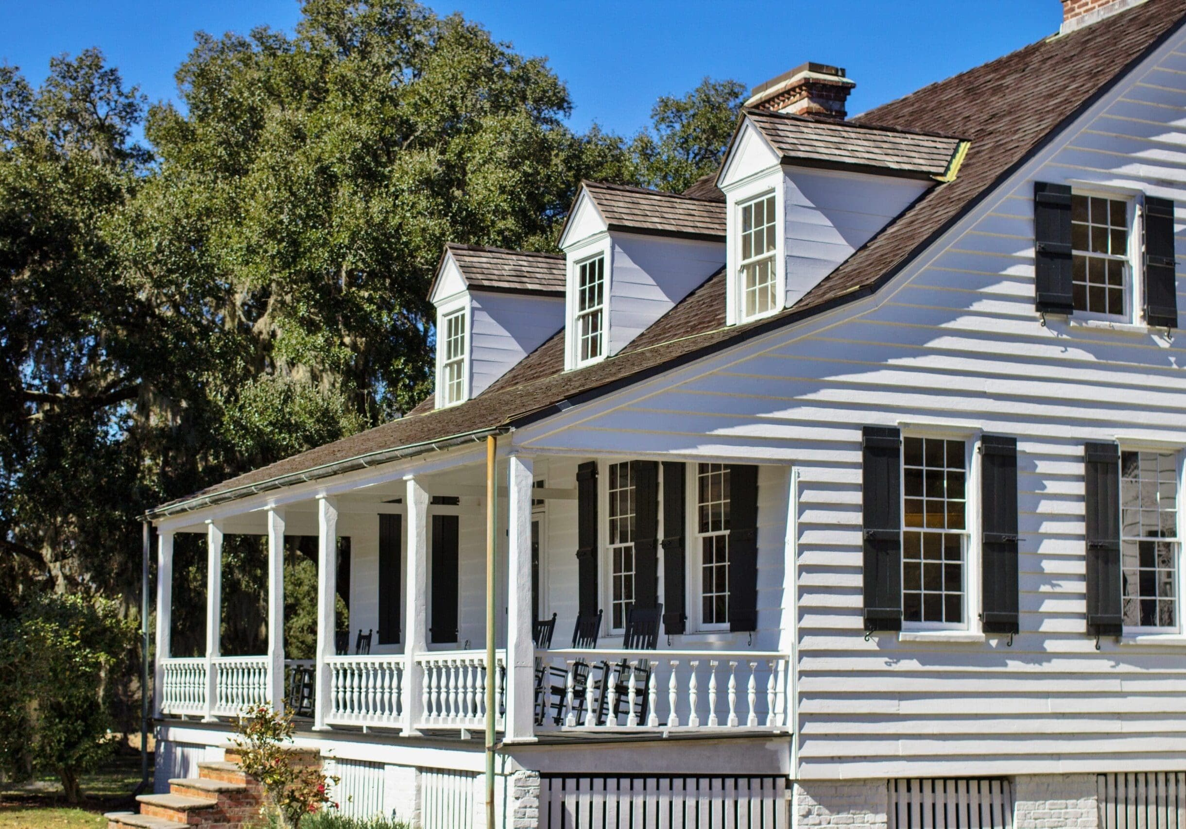 Historic white cottage with black shutters, double-hung windows, and a wraparound porch in Flowery Branch, Georgia.
