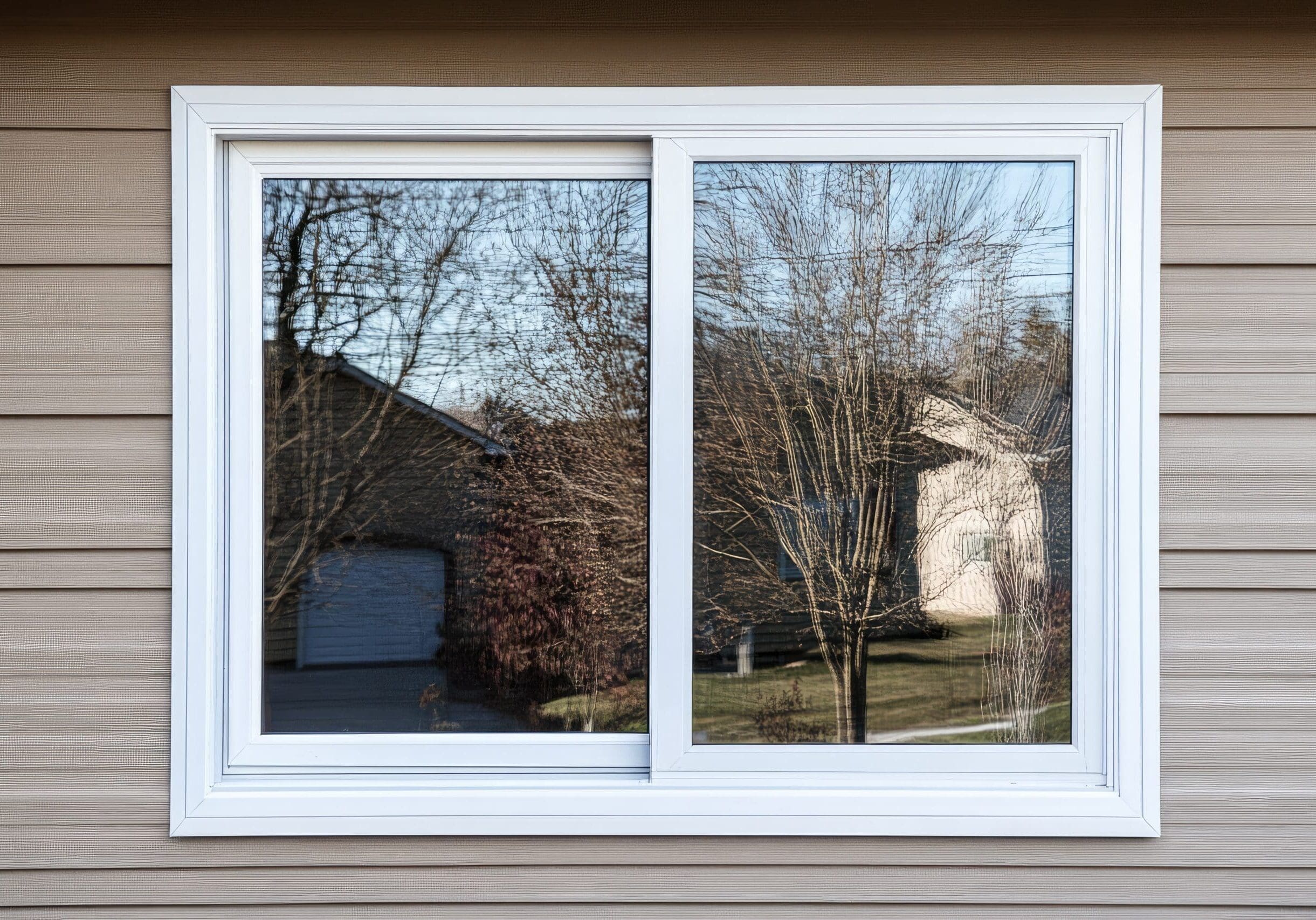 Exterior view of a white vinyl sliding window installed on a home with tan siding, showcasing the clean profile and dual-pane glass.