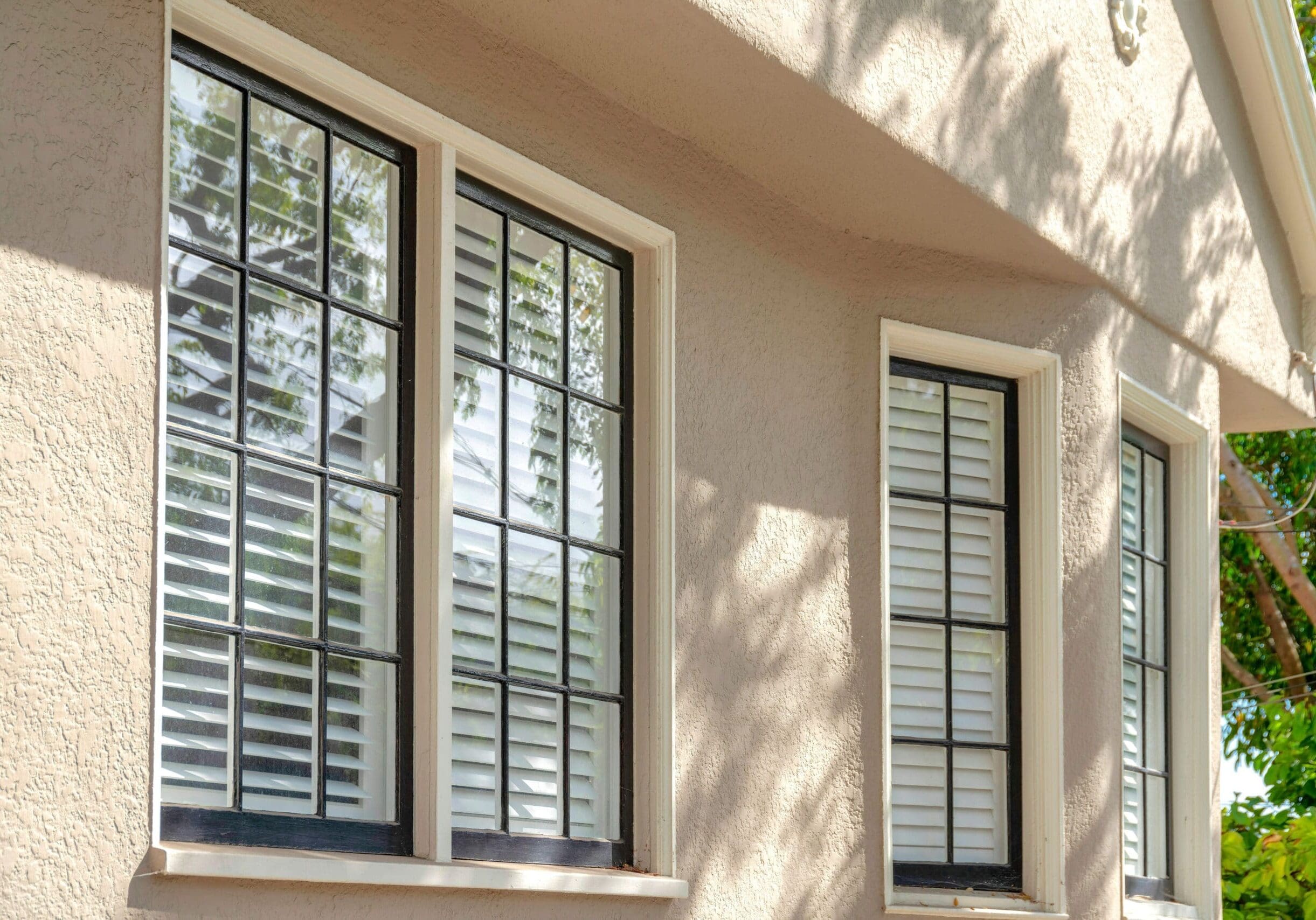 Three black-trim grid windows with white trim on a stucco home in Druid Hills, Georgia, reflecting trees and sky.