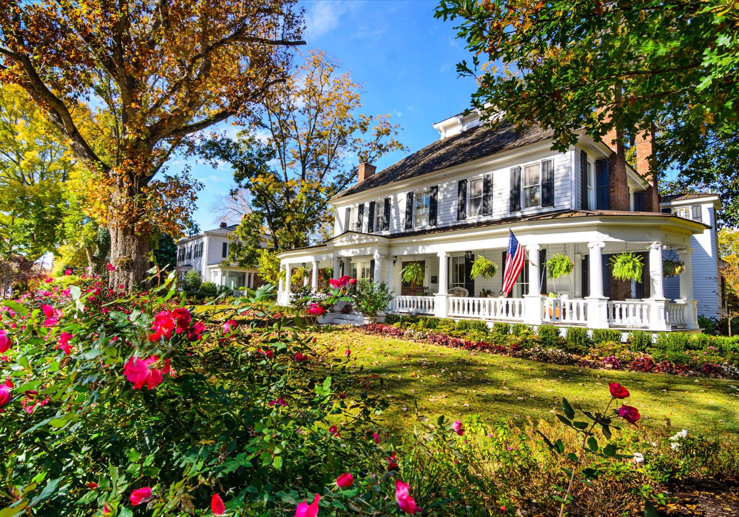 Historic white house with black shutters and tall windows in Lawrenceville, Georgia, surrounded by gardens and autumn trees.